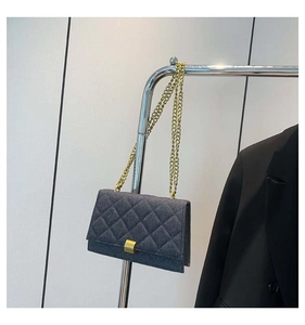 Detail of quilted denim shoulder bag with golden chain strap on a clothing rack