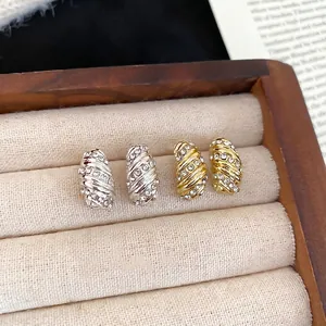 Elegant gold and silver wave stud earrings with cubic zirconia in a wooden jewelry box