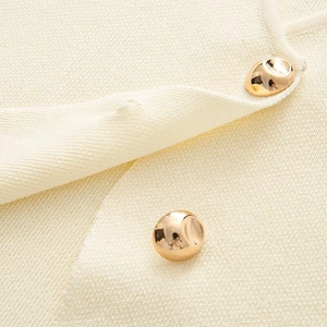 Close-up of knit fabric texture with two elegant golden metallic buttons on a beige vest