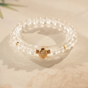Detail of clear crystal beaded bracelet with a gold clover charm on stone surface