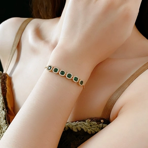 Close-up of a gold bracelet with square emerald-cut green zircons on a woman's wrist