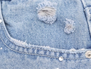 Détails macro du denim bleu clair avec déchirures stylées et clous en strass étincelants