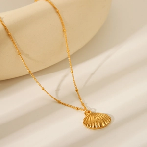Close-up of golden shell pendant necklace with delicate beaded chain in warm sunlight