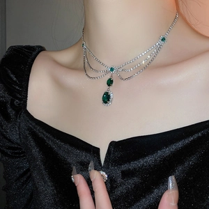 Macro detail of silver-tone layered necklace featuring emerald zircons on a model