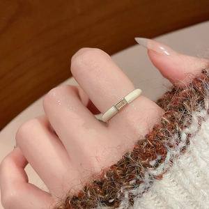 Macro detail of minimalist cream enamel square zircon ring on a soft knit background