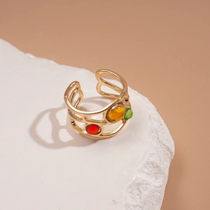 Gros plan d'une bague dorée réglable avec pierres précieuses colorées sur pierre blanche