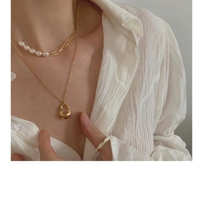 Detail of layered gold chain necklace with pearls and irregular pendant on a model