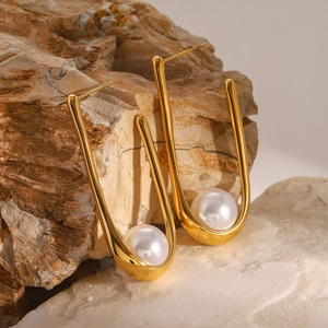 Macro shot of U-shaped gold earrings with white pearls resting on a natural stone background