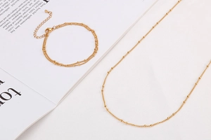 Golden double-layer bracelet and single necklace set on a magazine with lobster clasp details