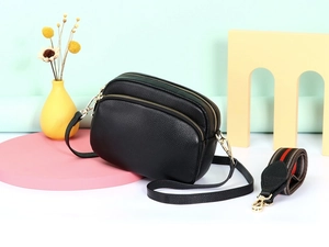 Detail van zwarte leren crossbodytas met drie ritsen en kleurrijke geweven schouderband