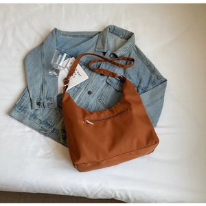 Detail of a brown nylon crescent bag with silver zipper on a blue denim jacket background