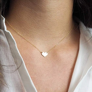 Gros plan d'un collier doré minimaliste doté d'un petit pendentif en forme de cœur sur une chaîne