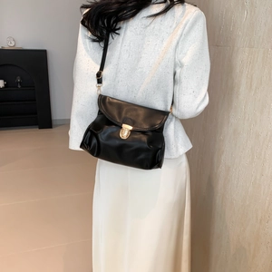 Minimalist black leather crossbody bag with gold clasp shown on model in a modern interior