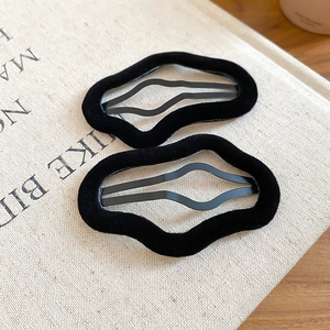 Close-up detail of two black flocked irregular wavy hair clips on a soft fabric surface