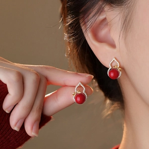 Detail of red gourd earrings with golden bow and pavé zircon stones on earlobe