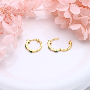 Macro detail of gold huggie earrings with alternating green and white gemstones