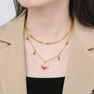 Detail of double-layer gold necklace with red heart pendant and evil eye design on model