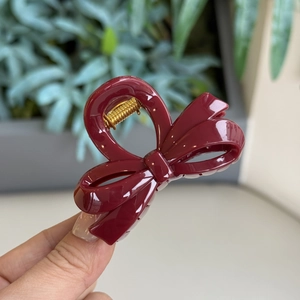 Detail shot of a wine red bow hair claw clip made of glossy resin with a gold metal spring