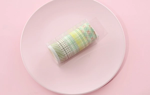 Close-up of 6-roll green plaid washi tape set in transparent box on pink background