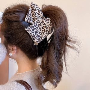Detailed close-up of a vintage leopard print bow hair clip on long wavy brown hair