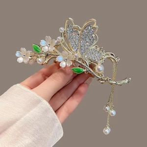 Detailed close-up of gold flower hair claw with rhinestone butterfly and pearl tassels