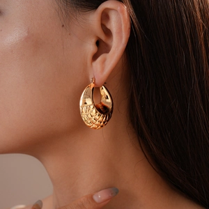 Detailed close-up of a large gold hoop earring featuring a unique mesh texture on a model