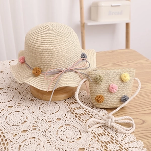 Close-up of kids straw hat and crossbody bag set with colorful pom-poms and wavy brim