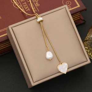 Golden pearl heart pendant necklace on a beige jewelry box with vintage book props