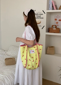 Detail of a large yellow plaid tote bag with red bow prints and FUTURE text on its front