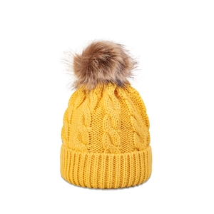 Detailed cable knit texture of a yellow winter beanie with a soft faux fur pom-pom