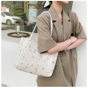 Close-up of woven straw tote bag with delicate green leaf embroidery and rope handles