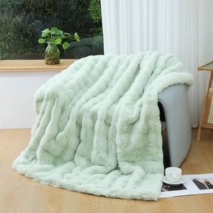 Detail of mint green faux fur blanket with thick stripe texture on a grey leather chair