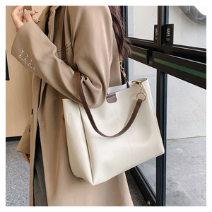 Close-up of stylish cream leather tote bag with brown straps and gold metal ring details