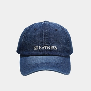 Detailed close-up of white 3D embroidery showing GREATNESS on blue denim baseball cap