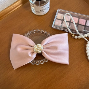 Detailed shot of a pink satin bow hair clip with pearl flower on a vanity setup