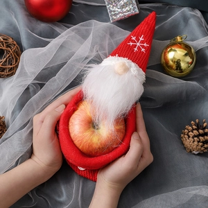 Knitted faceless Christmas gnome candy bag being held with holiday decorations