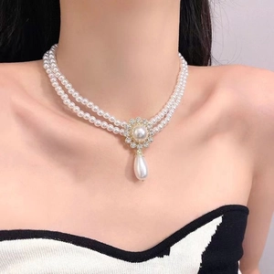 Detail of a double-layered pearl necklace with flower and teardrop pendants on a model