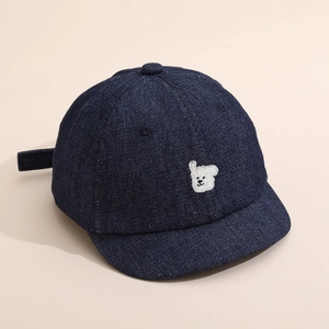 Gros plan détaillé sur la broderie ours et la texture denim bleu marine de la casquette enfant