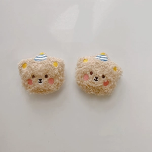 Close-up of two beige plush bear accessories with embroidery and striped hats