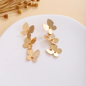 Detailed close-up of three-tier gold butterfly drop earrings on a white display tray