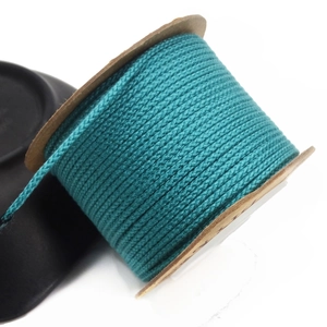 Macro detail of 1.5mm lake blue braided cotton cord neatly wound on a paper spool