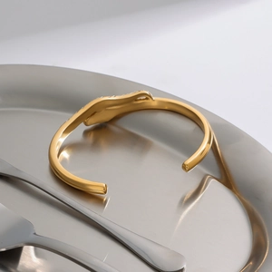 Macro shot of gold snake bracelet with zircon inlay on a sleek metal tray decor