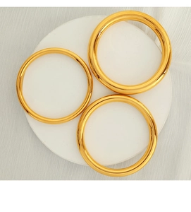Detailed view of three polished 18K gold-plated minimalist bangles on a white display