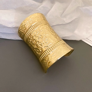 Primer plano de la pulsera dorada ancha con motivos florales en relieve y bordes de perlas