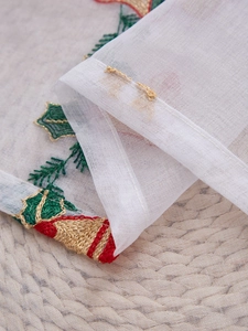 Macro detail of Christmas holly and bell embroidery on white translucent tulle fabric
