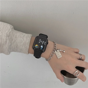 Close-up of black digital watch with LED display and silicone strap on wrist with jewelry