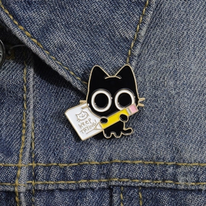 Detail of cute black cat enamel pin with pencil and Keep Trying text on denim