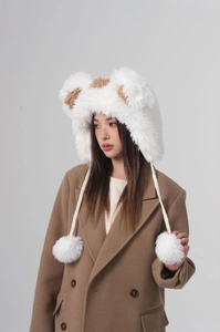 Detail of plush bear ear hat with white pompoms and long braided ties on a female model