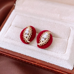 Detail of oval gold earrings with three pearls and crystal rhinestones on red velvet