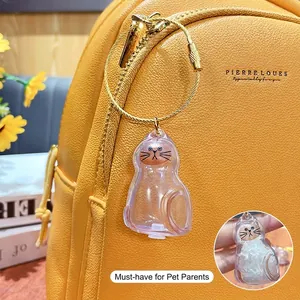 Transparent cat-shaped capsule keychain for pet hair storage on a yellow leather bag